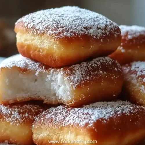 Stack of golden air fryer beignets topped with powdered sugar on wooden board