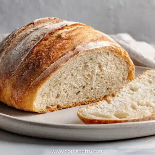 rustic round bread loaf with golden crust and airy crumb on ceramic plate