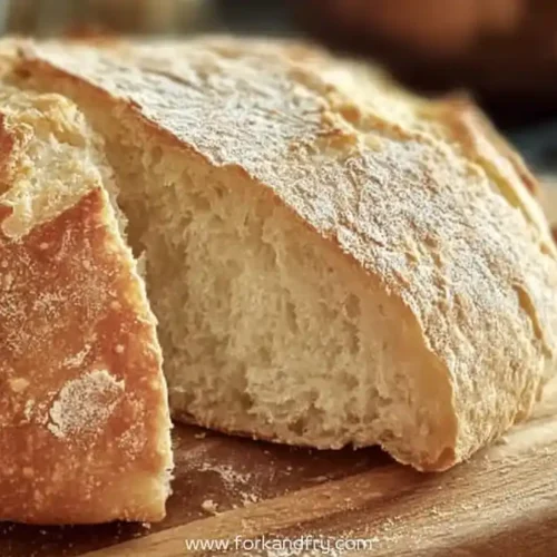 golden crusty artisan bread with soft fluffy interior on wooden board dusted with flour