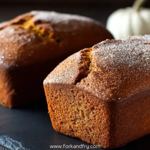 Mini pumpkin bread loaves dusted with sugar on slate board with soft background of white pumpkins